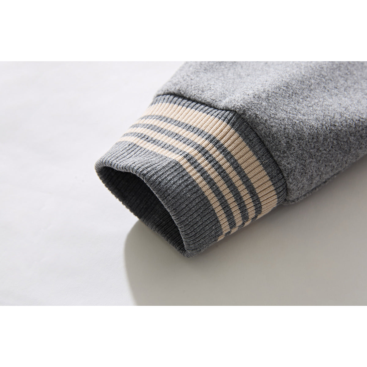 Close-up of a gray jacket sleeve ending in a ribbed cuff with cream and charcoal stripes.