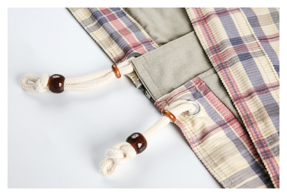 Close-up of cream plaid garment with white drawcords, dark beads, metal eyelets, and a beige fastening panel.