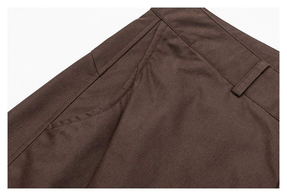 Close-up of dark brown trousers showing a curved pocket opening, seams, and a belt loop.