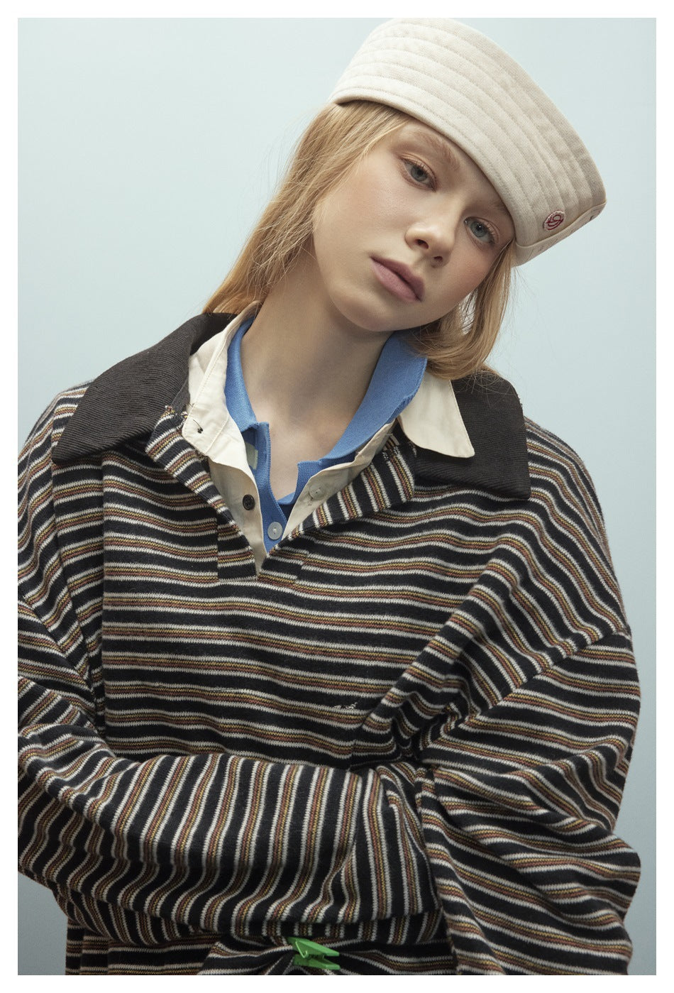 Close view of a model in an oversized dark striped polo with a cream collar and a cream padded cap.