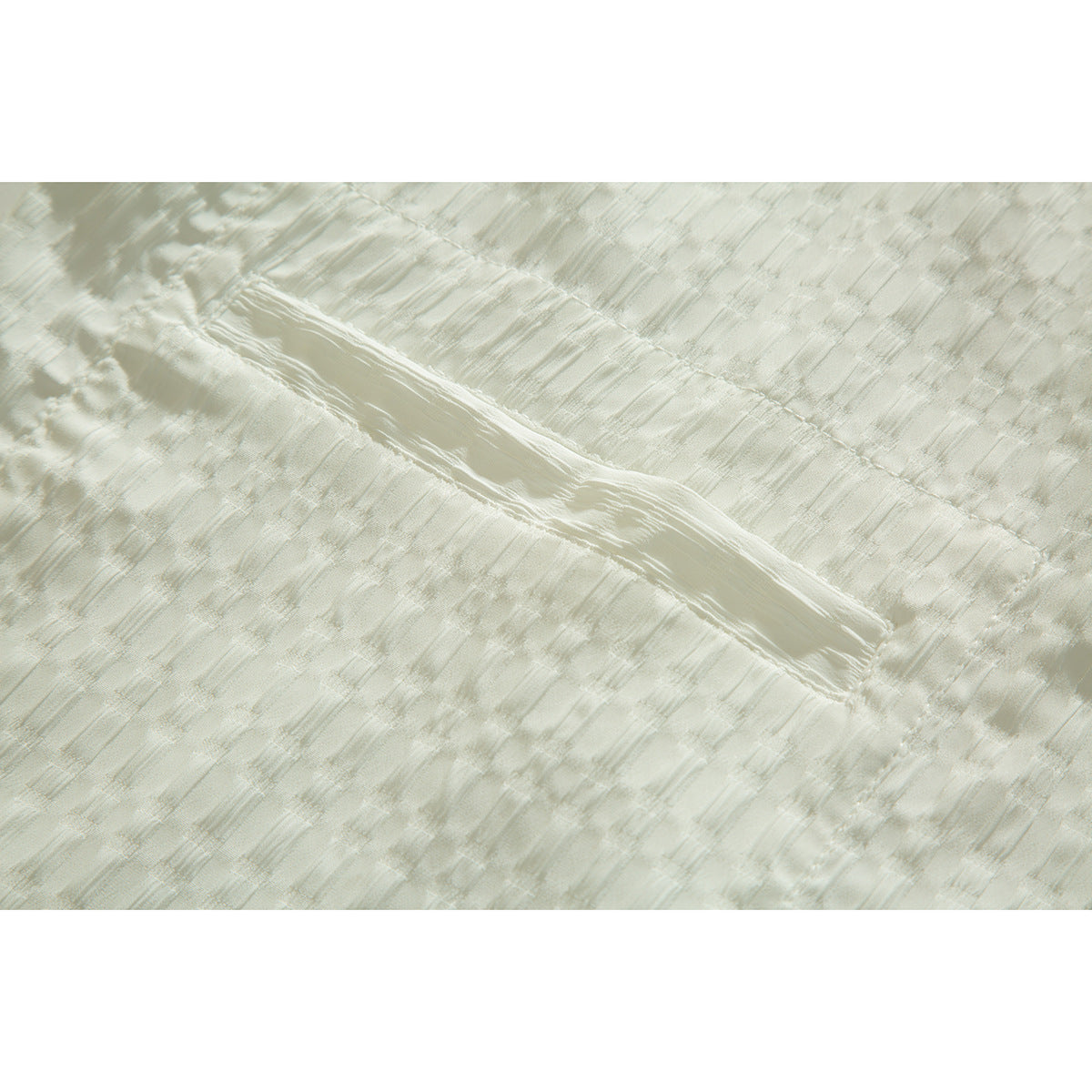 Close-up of a stitched seam and textured ivory fabric on a shirt.