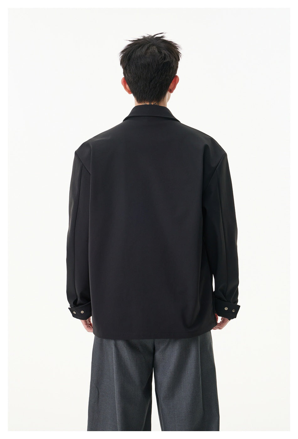 Back view of a model wearing a black jacket with a pointed collar and buttoned cuffs.
