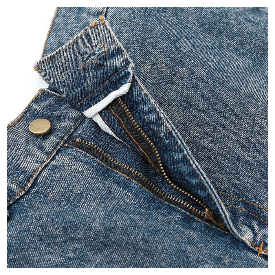 Close-up of blue denim waistband opened to show a brass-tone button and exposed zipper fly.