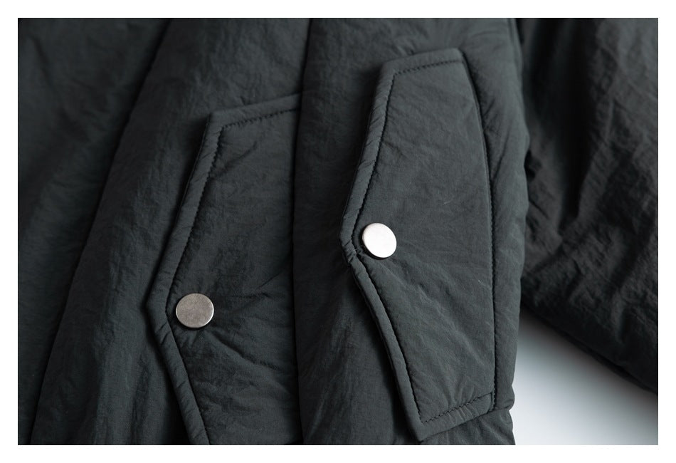 Close-up of a black jacket with two angular flap pockets and round metal snap fasteners.