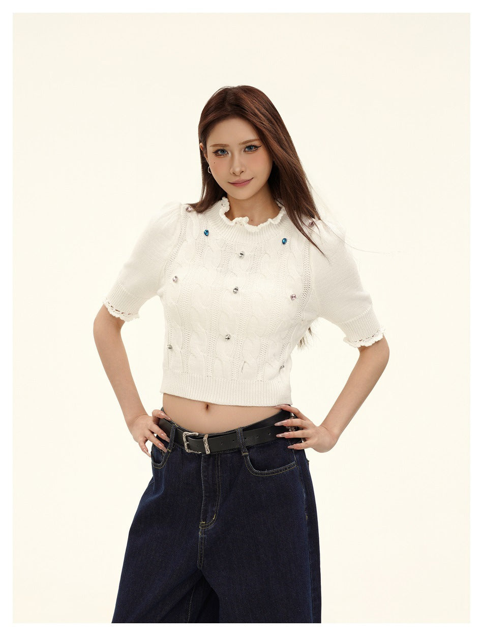 Model in an ivory cable-knit cropped top with jeweled accents and scalloped trim, styled with dark jeans.
