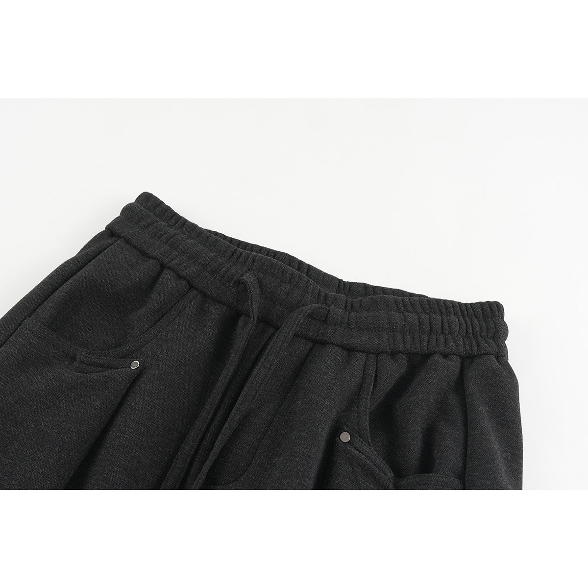 Close-up of charcoal wide-leg pants showing the elastic drawstring waistband and angled front pockets with metal rivets.