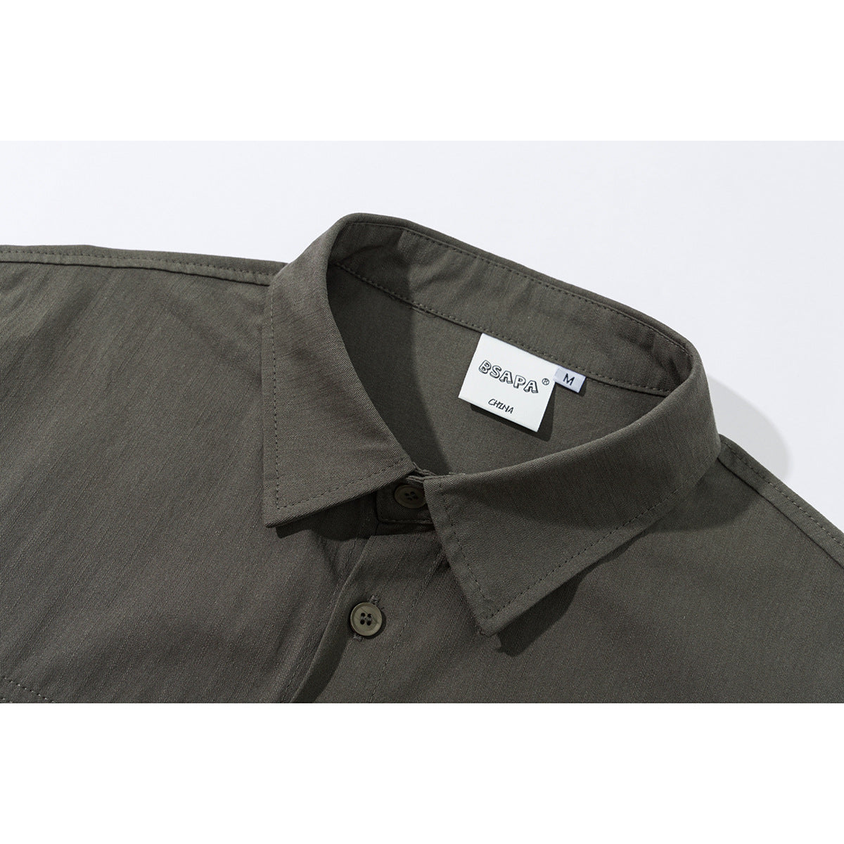 Close-up of an olive-gray short-sleeve shirt collar, buttons, stitching, and neck label.