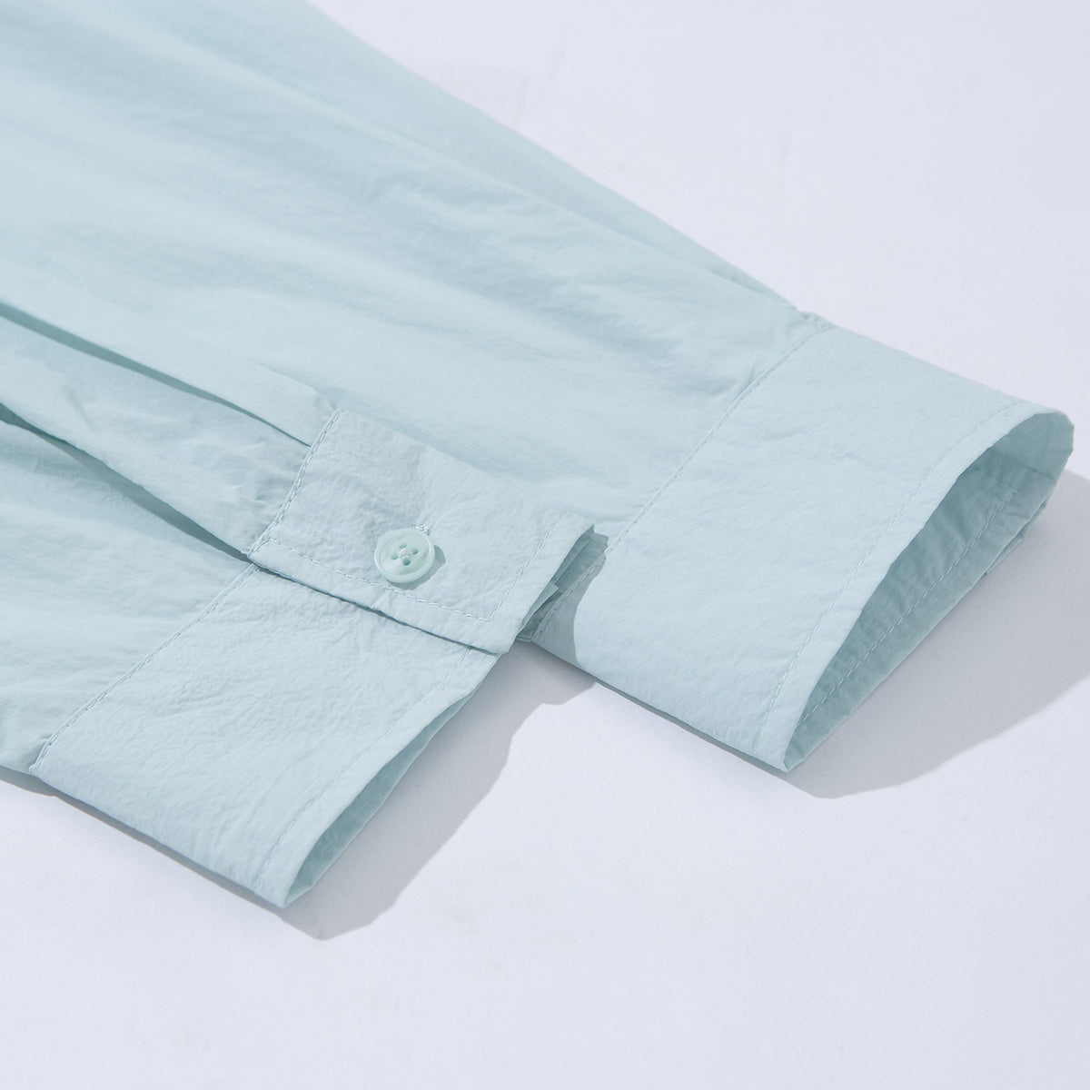 Close-up of a pale aqua shirt sleeve ending in a buttoned cuff.