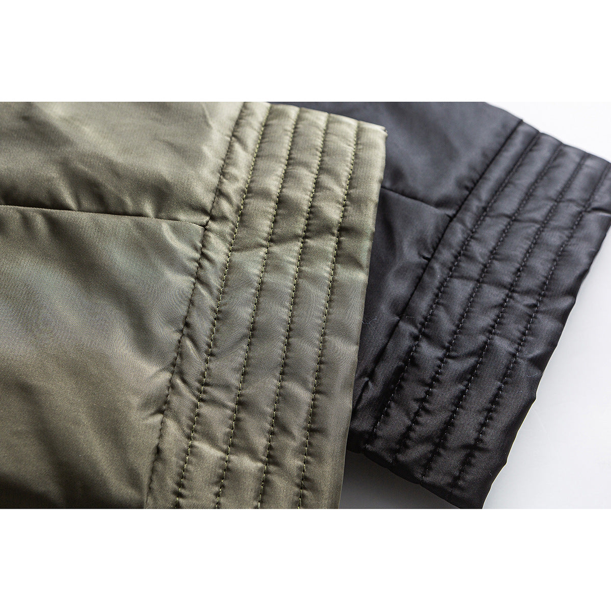 Close-up of olive and black jacket sleeves with parallel quilted stitching.