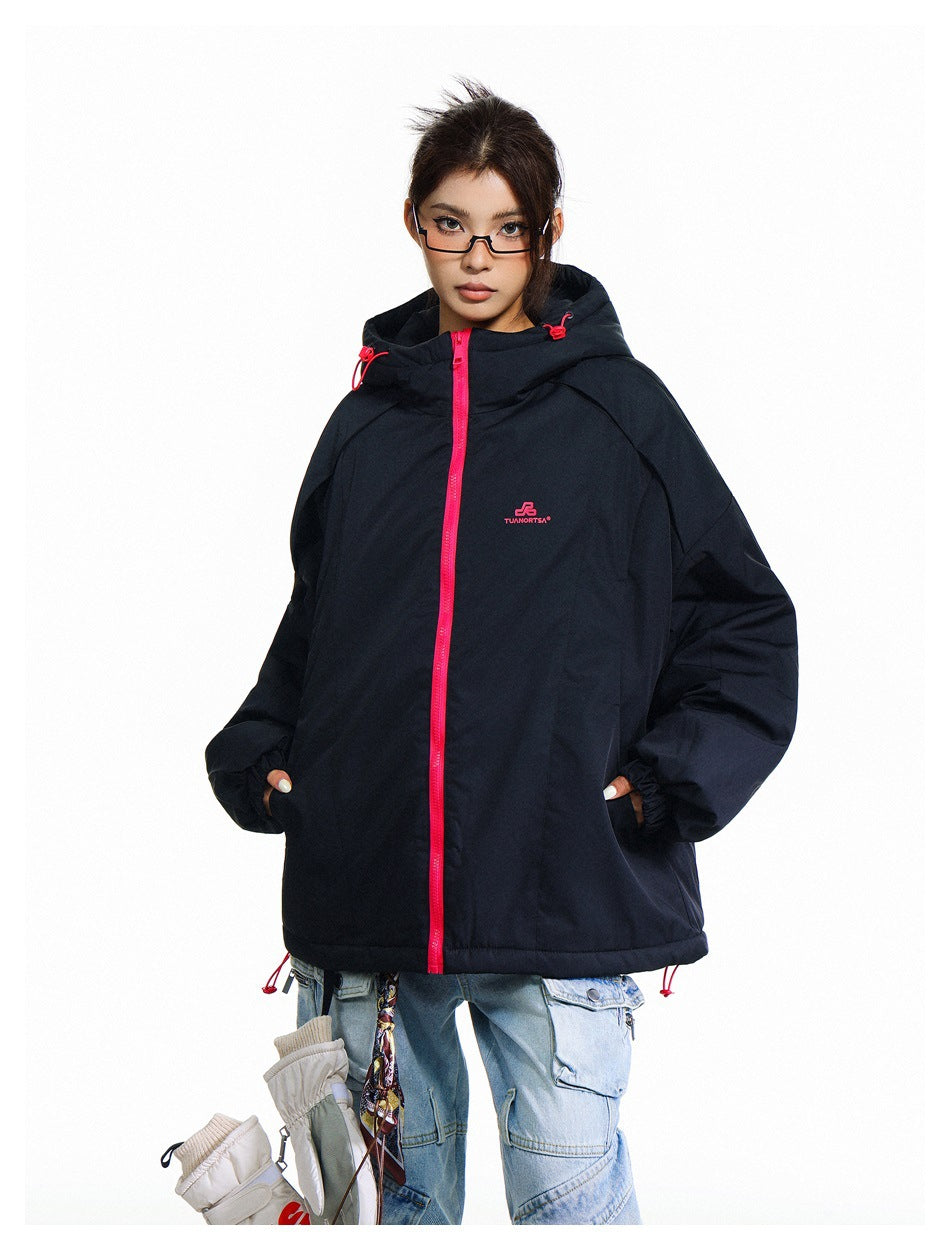 Model wearing an oversized black hooded jacket zipped closed with a bright pink front zipper.