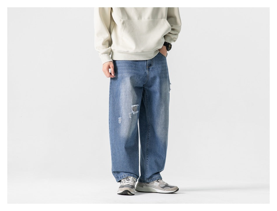 Person wearing blue faded wide-leg ripped jeans with a cream hoodie and gray sneakers, angled view, cropped at the chest
