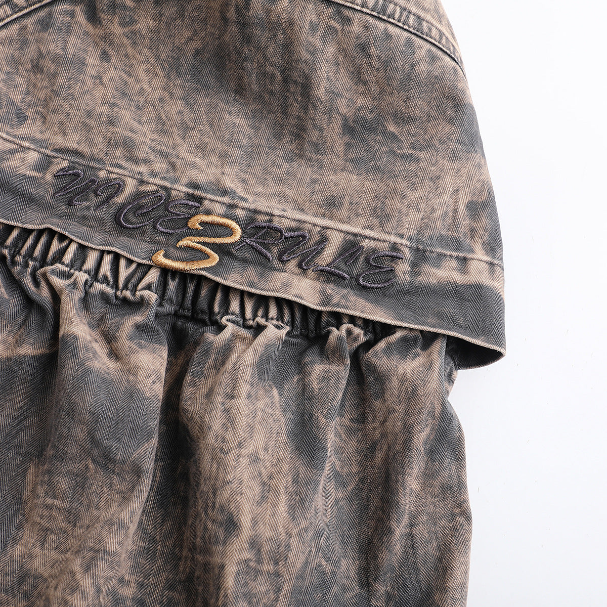 Close-up of dark and gold decorative embroidery on a brown-gray patterned garment panel.