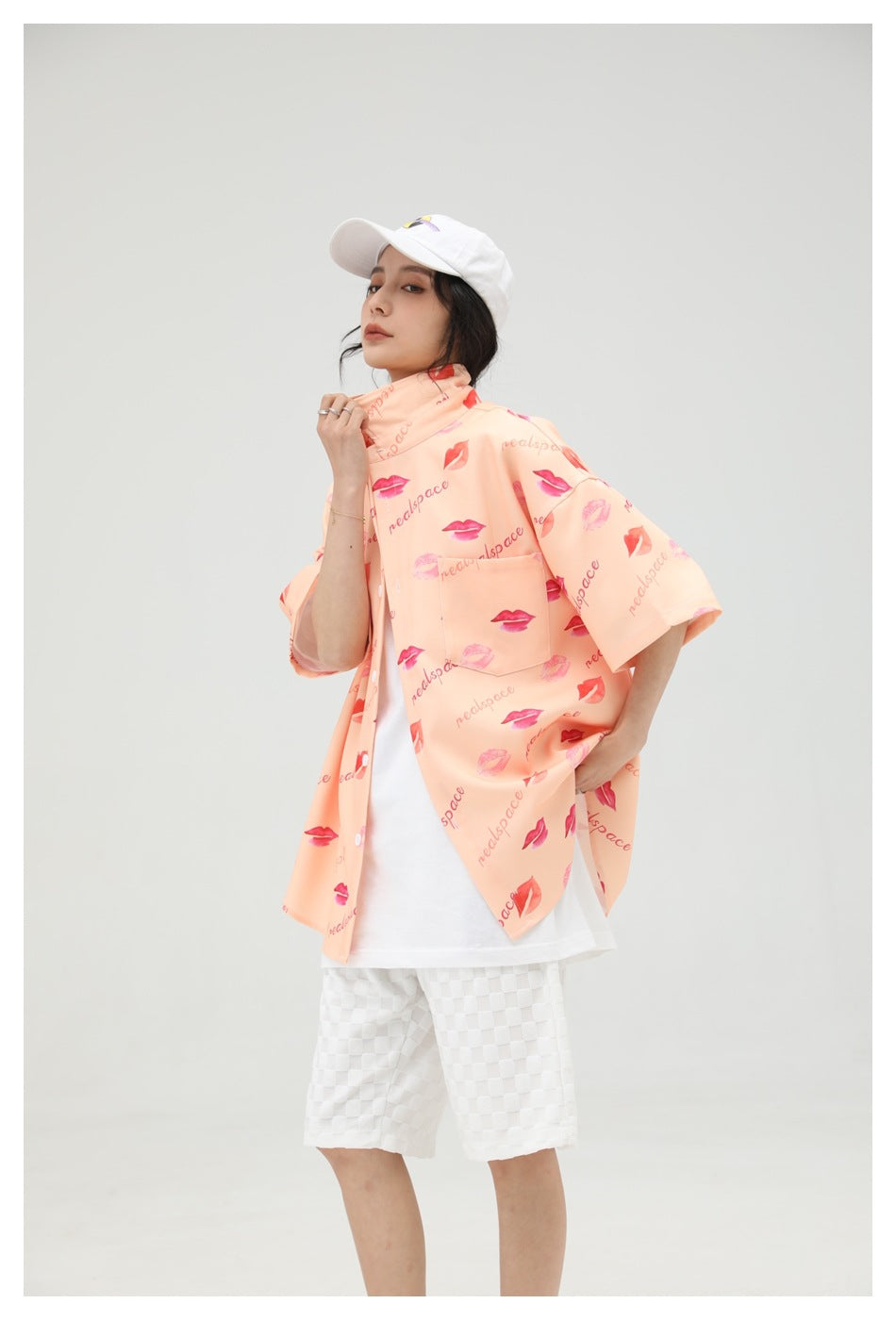 Angled view of a model wearing the peach printed short-sleeve shirt over a white top and checkered shorts.