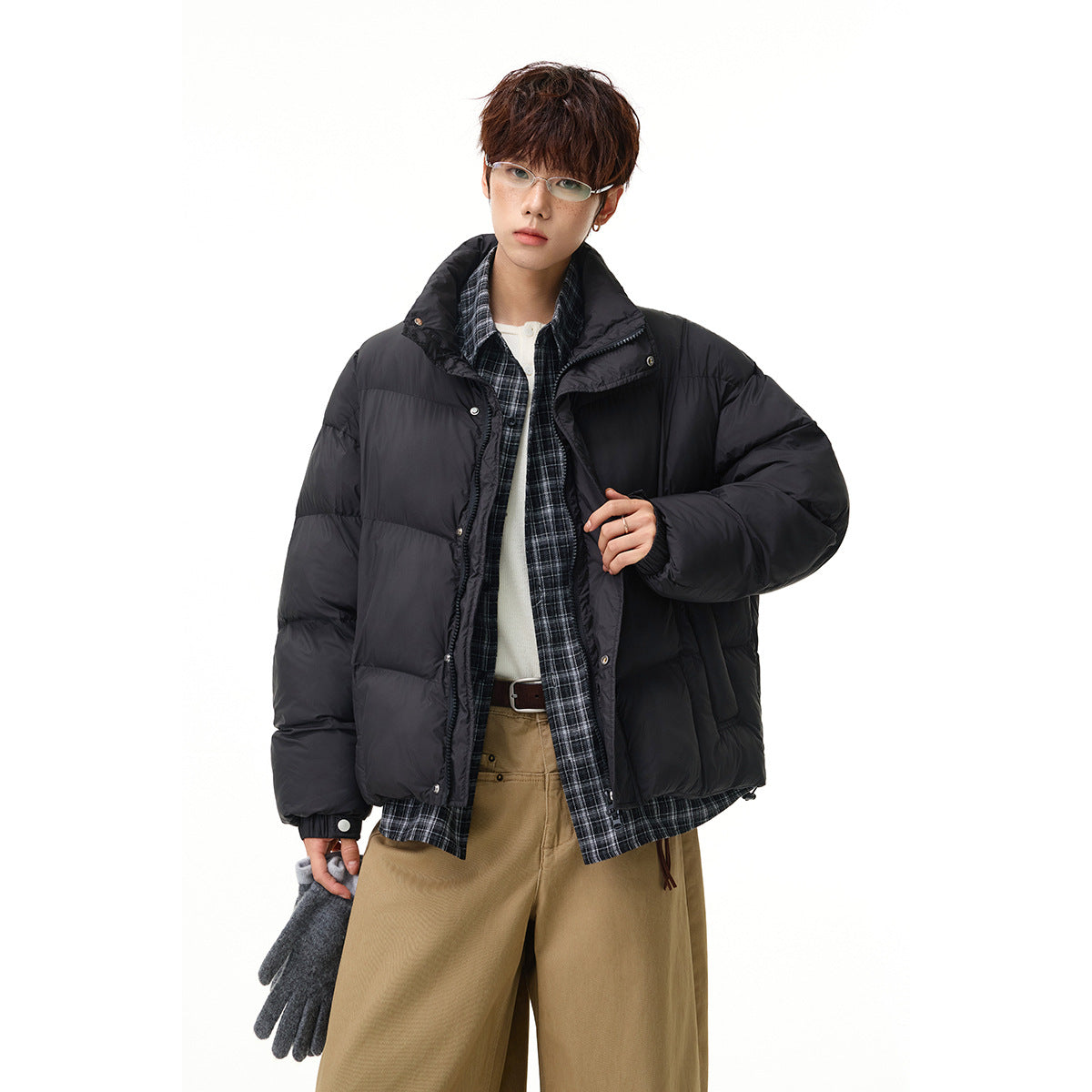 Closer view of a model wearing an open black quilted puffer jacket over a dark plaid shirt.