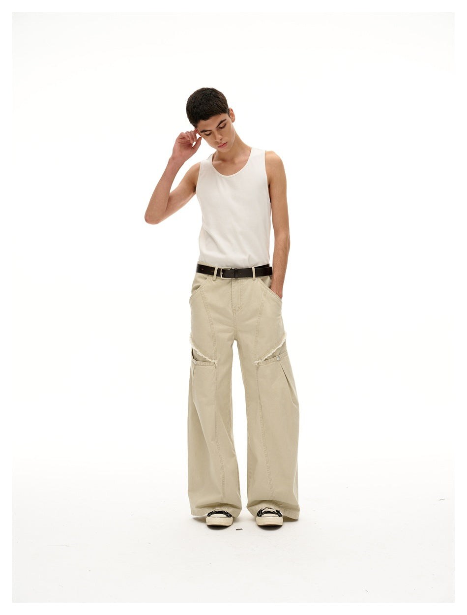 Model wearing a white tank top and light beige wide-leg pants with buttoned knee panels and a black belt.