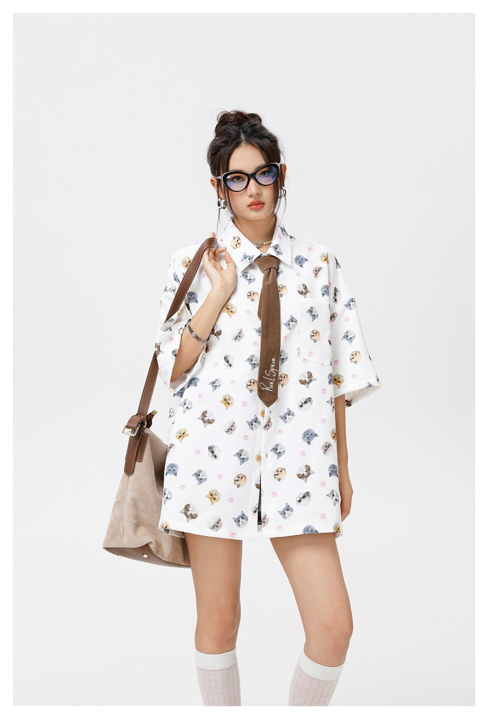 Model wearing a white oversized short-sleeve shirt with scattered cat faces and pink paw prints, shown from the front.
