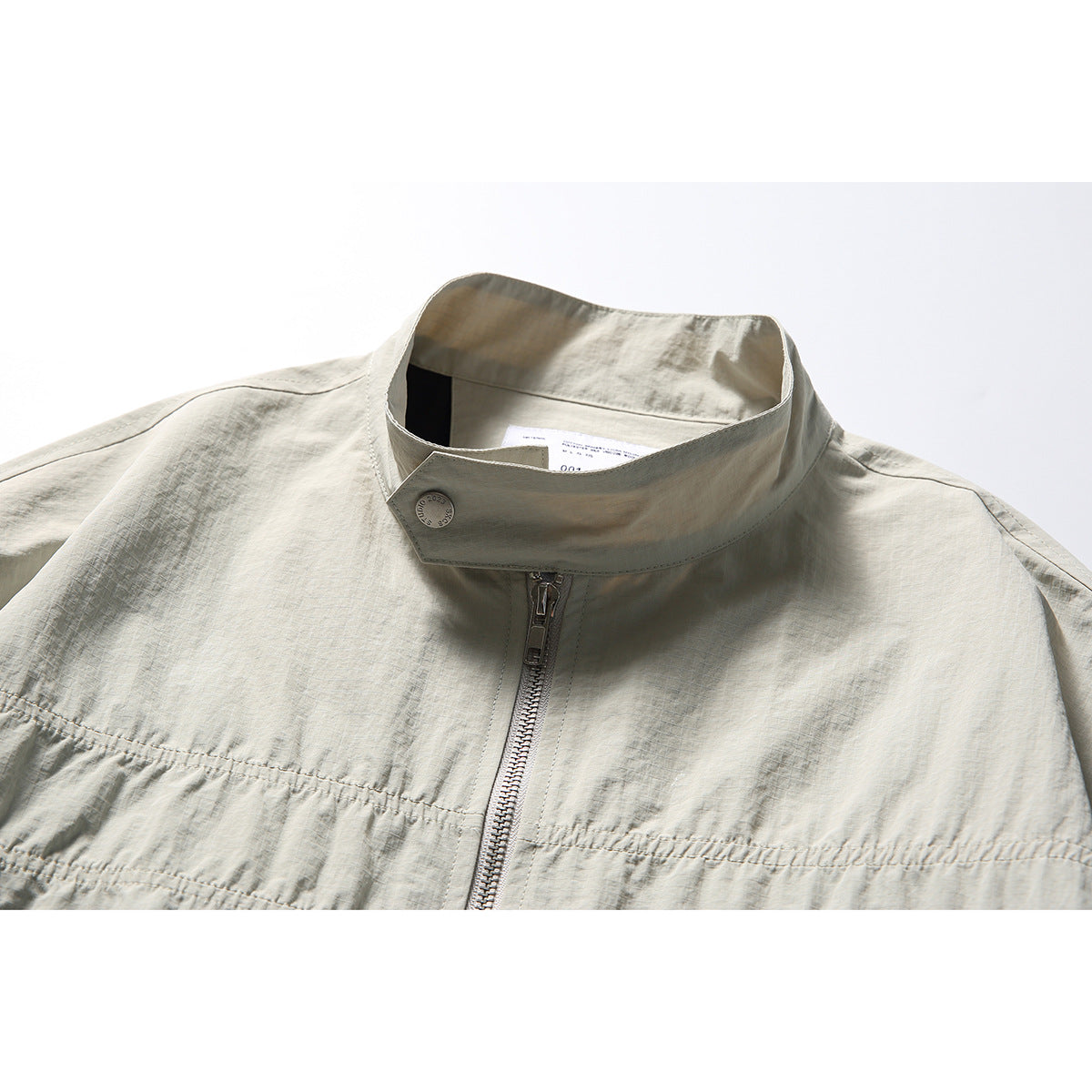 Close-up of a light gray-beige jacket collar, snap tab, zipper and chest seam.