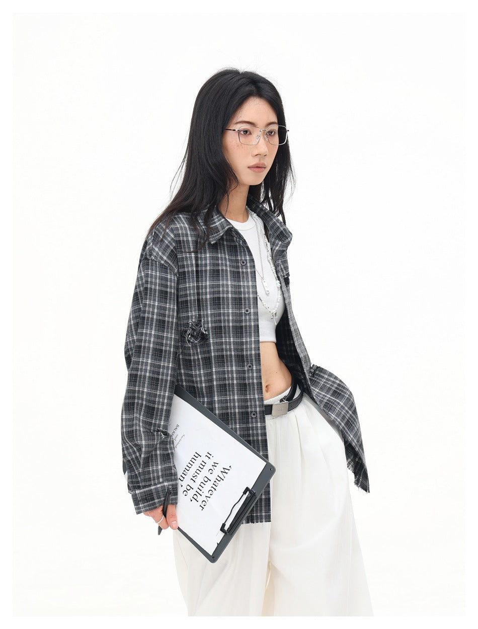 Three-quarter view of a model wearing an open charcoal gray plaid shirt over a white top and trousers.
