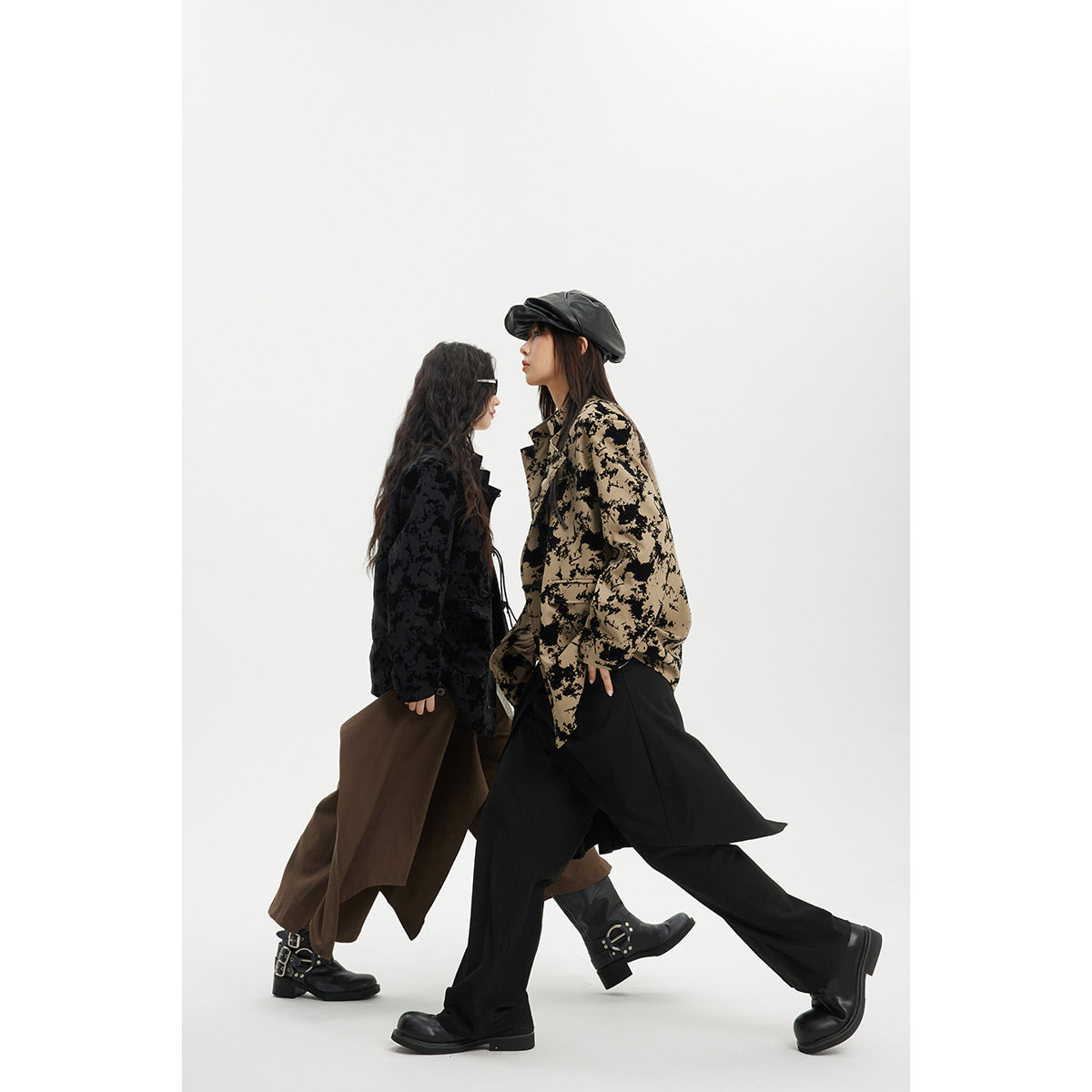 Two models walk in profile wearing oversized abstract-patterned jackets in black and tan, with loose trousers.