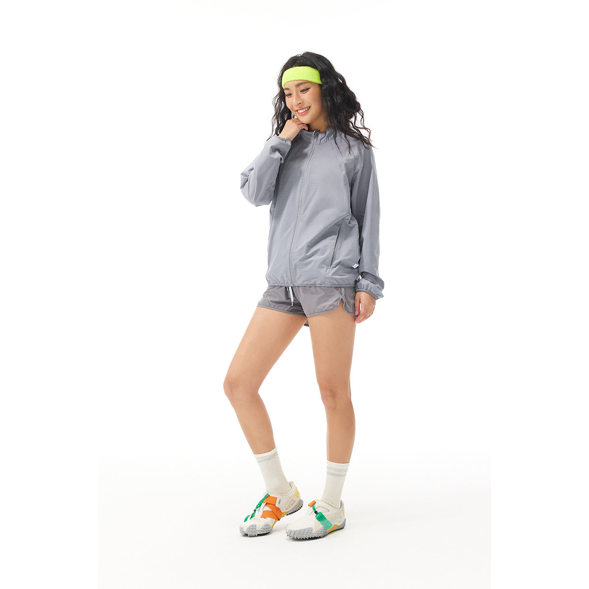 Model wearing a light gray zip jacket and matching shorts with a neon yellow headband.