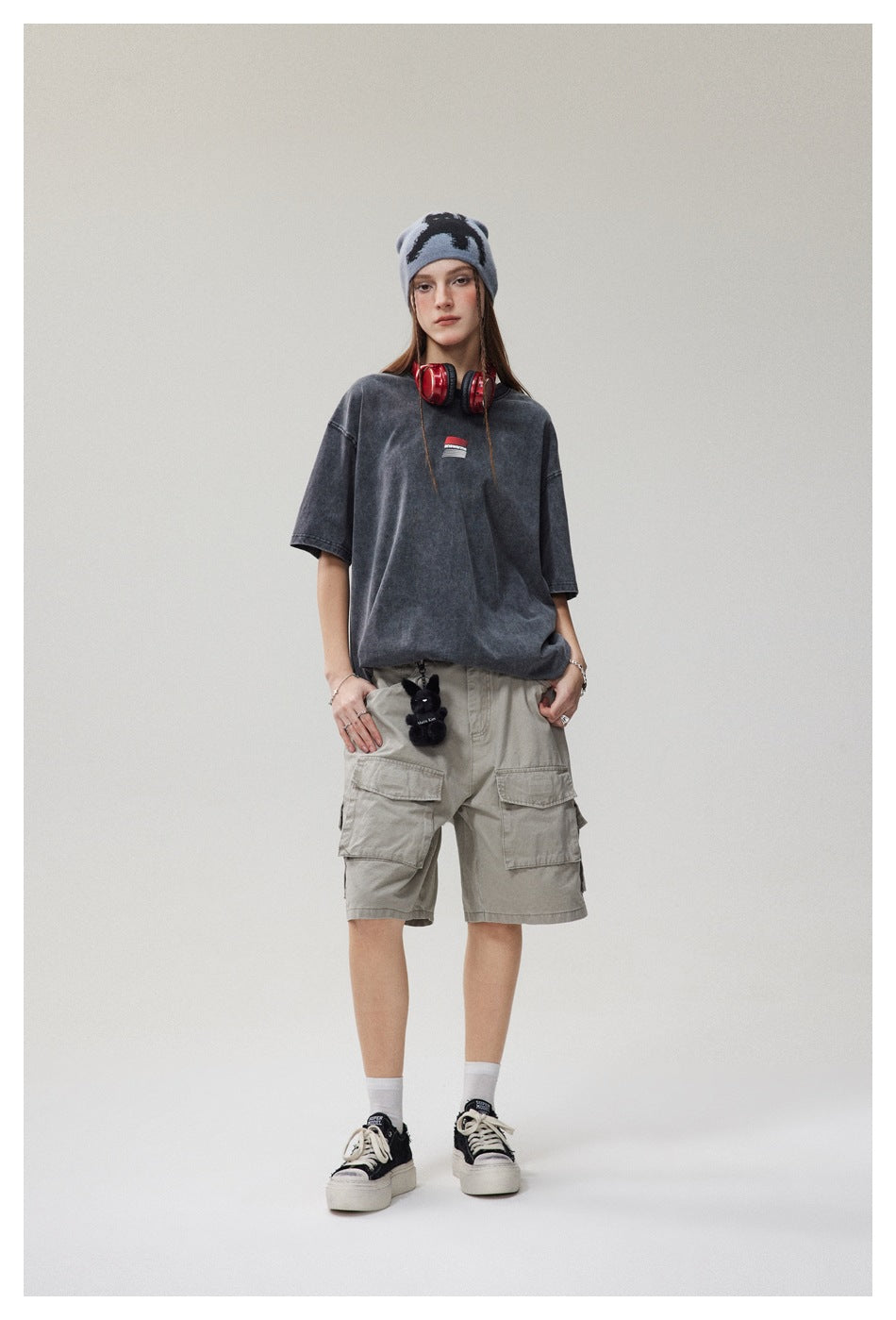 Full-length model wearing an oversized faded charcoal T-shirt with a small chest graphic and light gray cargo shorts.
