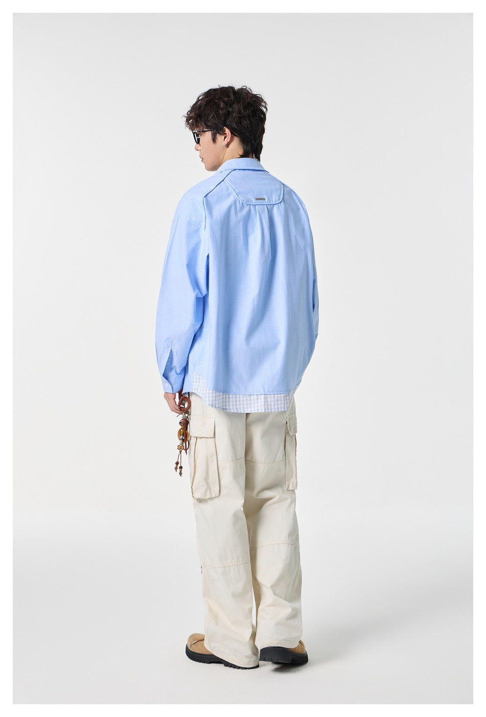 Rear view of a model wearing a light blue shirt with a plaid hem and cream cargo pants.