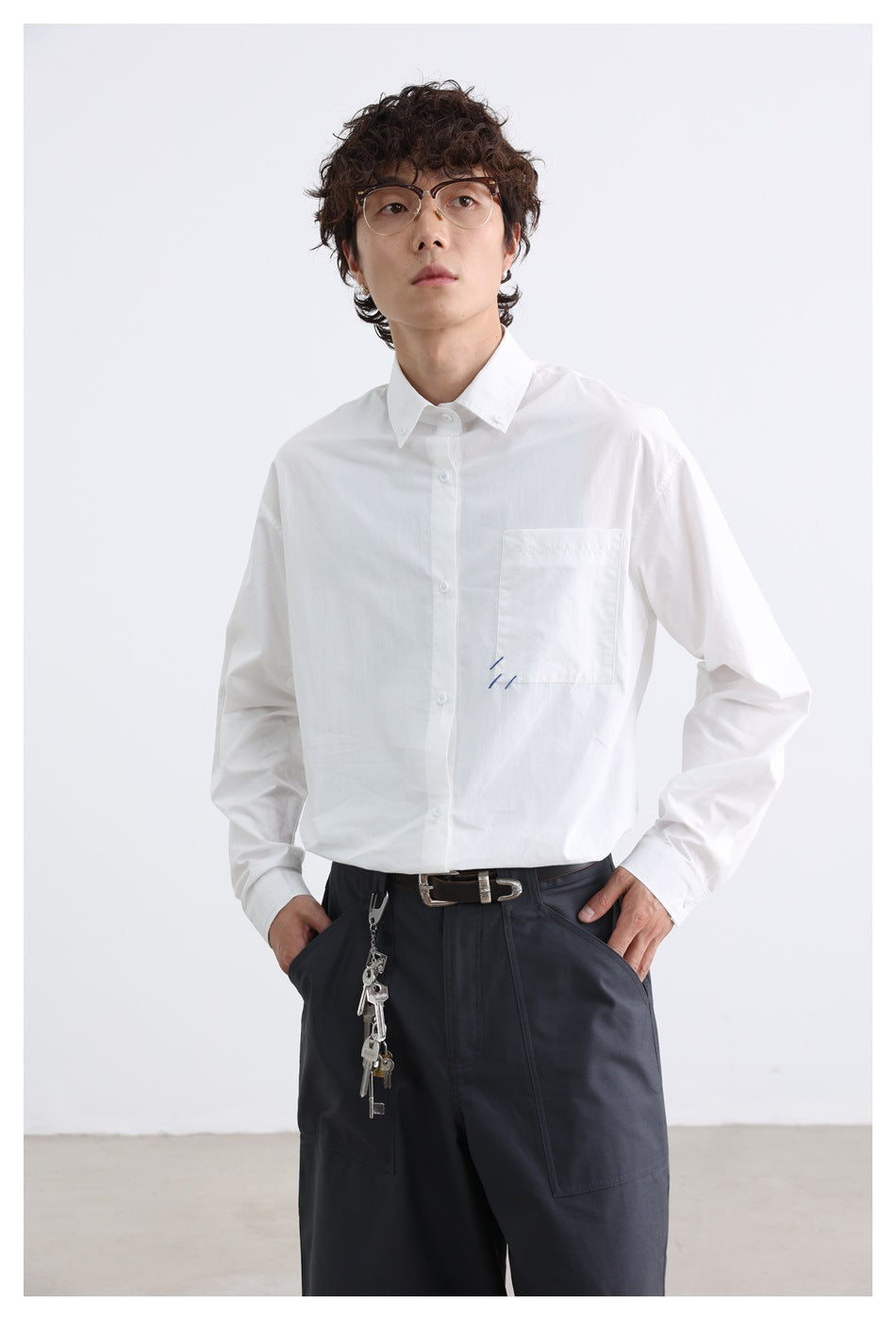 Closer front view of a model wearing a white button-up shirt with a chest pocket and small blue stitch accents.