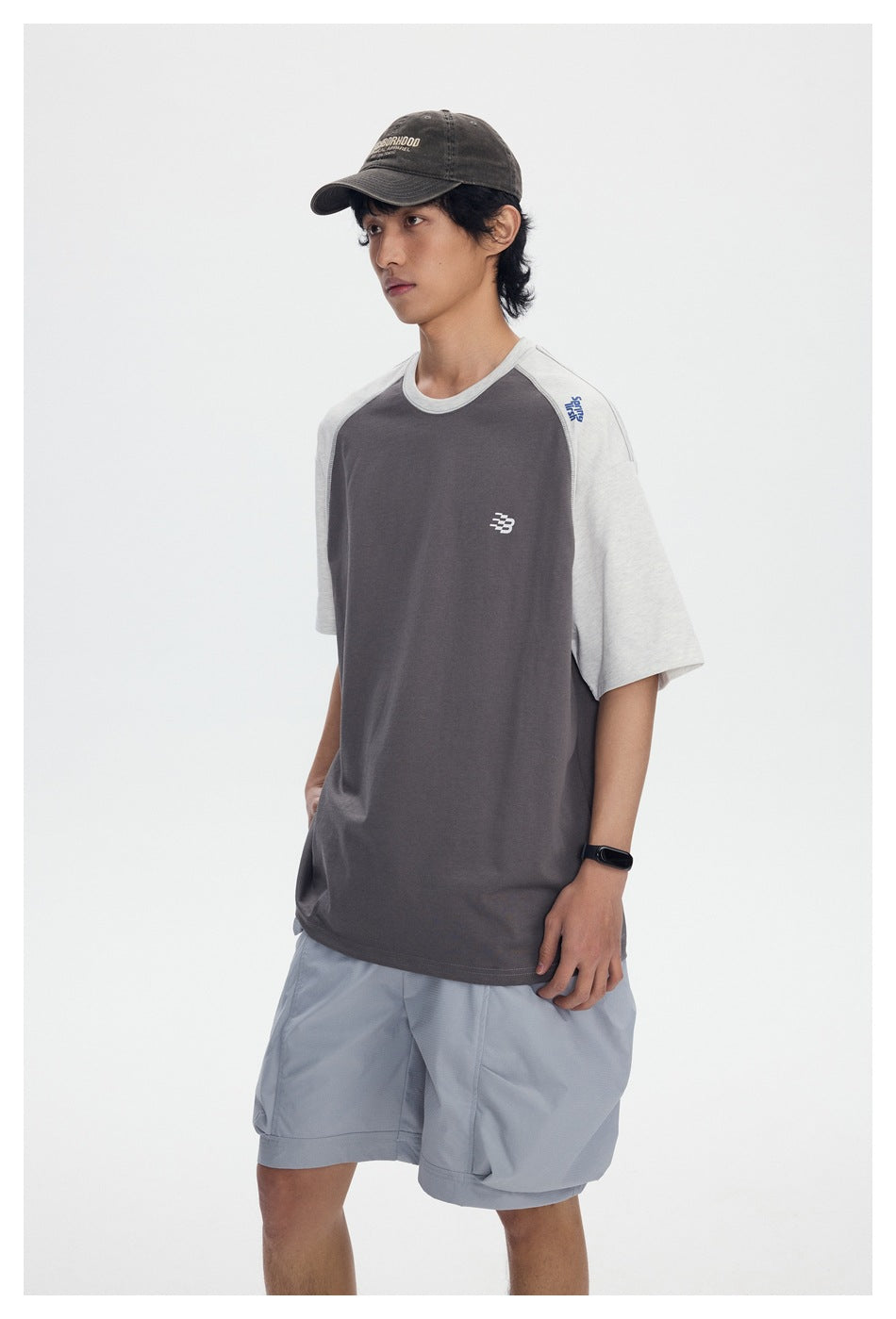 Three-quarter view of a model wearing a charcoal T-shirt with light gray raglan sleeves.