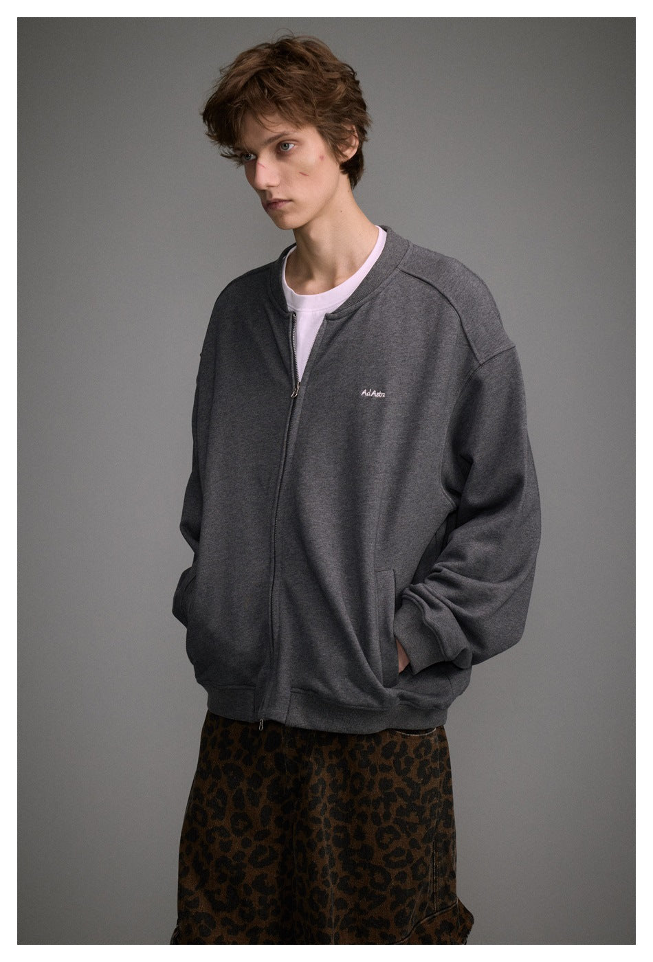 Closer view of a model wearing a charcoal gray zip-front jacket with small chest embroidery and brown leopard-print pants.