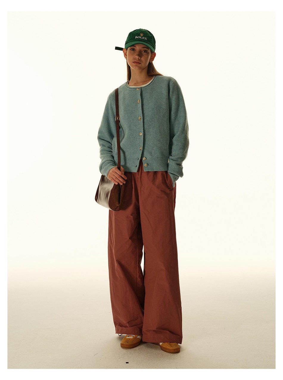 Model wearing a pale blue button-front cardigan, rust-brown wide-leg trousers, and a green cap.