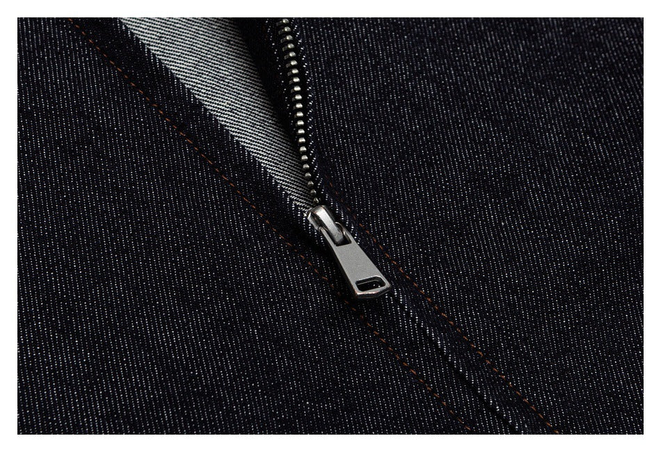 Close-up of a metal zipper and orange stitching on dark indigo denim.