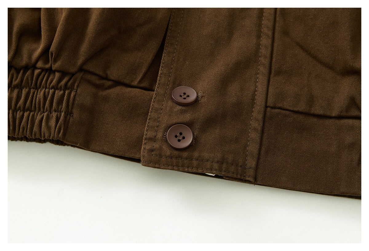 Close-up of a dark brown jacket hem with gathered elastic and two brown buttons on a flap.