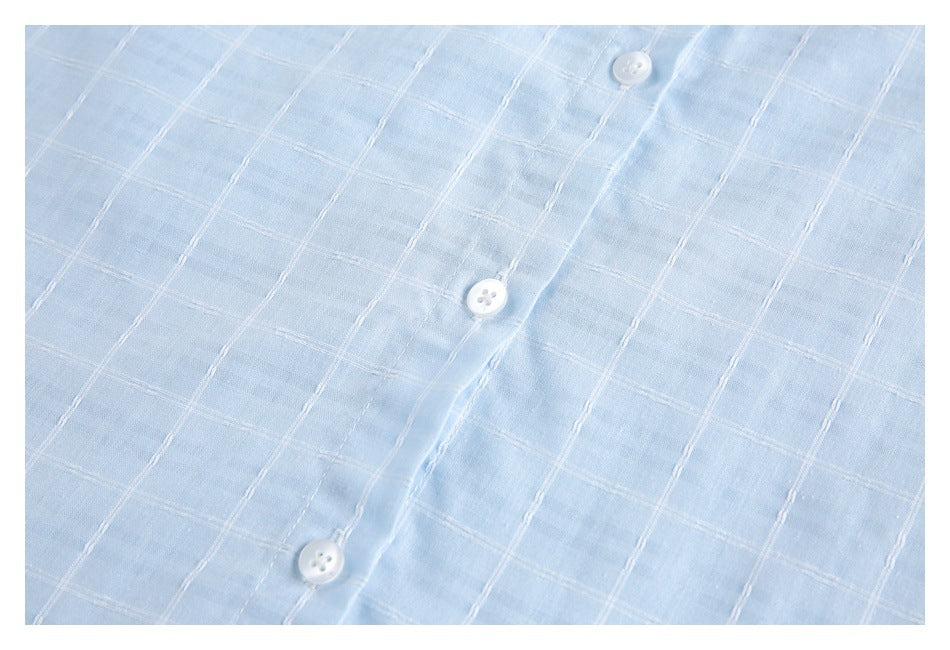 Close-up of the pale blue shirt front, showing white buttons and white windowpane stitching.