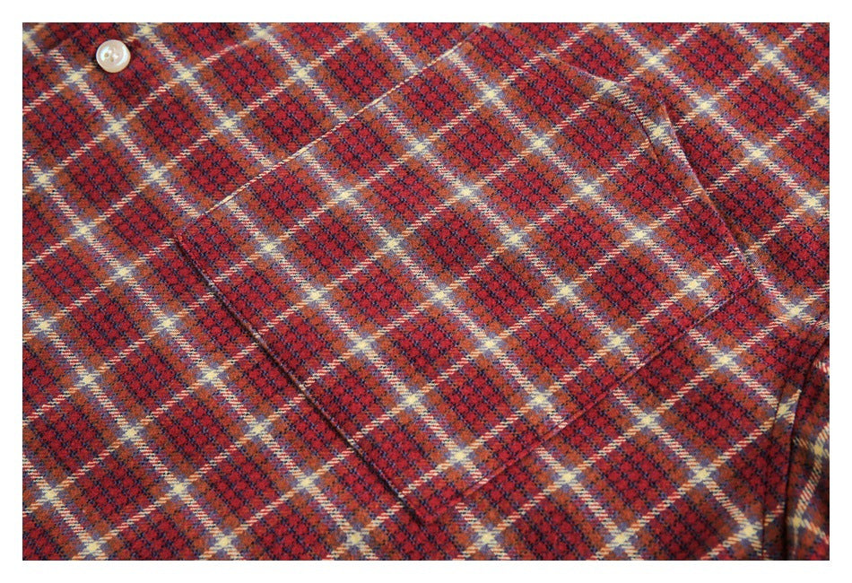 Close-up of red, navy, and cream plaid shirt fabric showing a button and pocket seam.