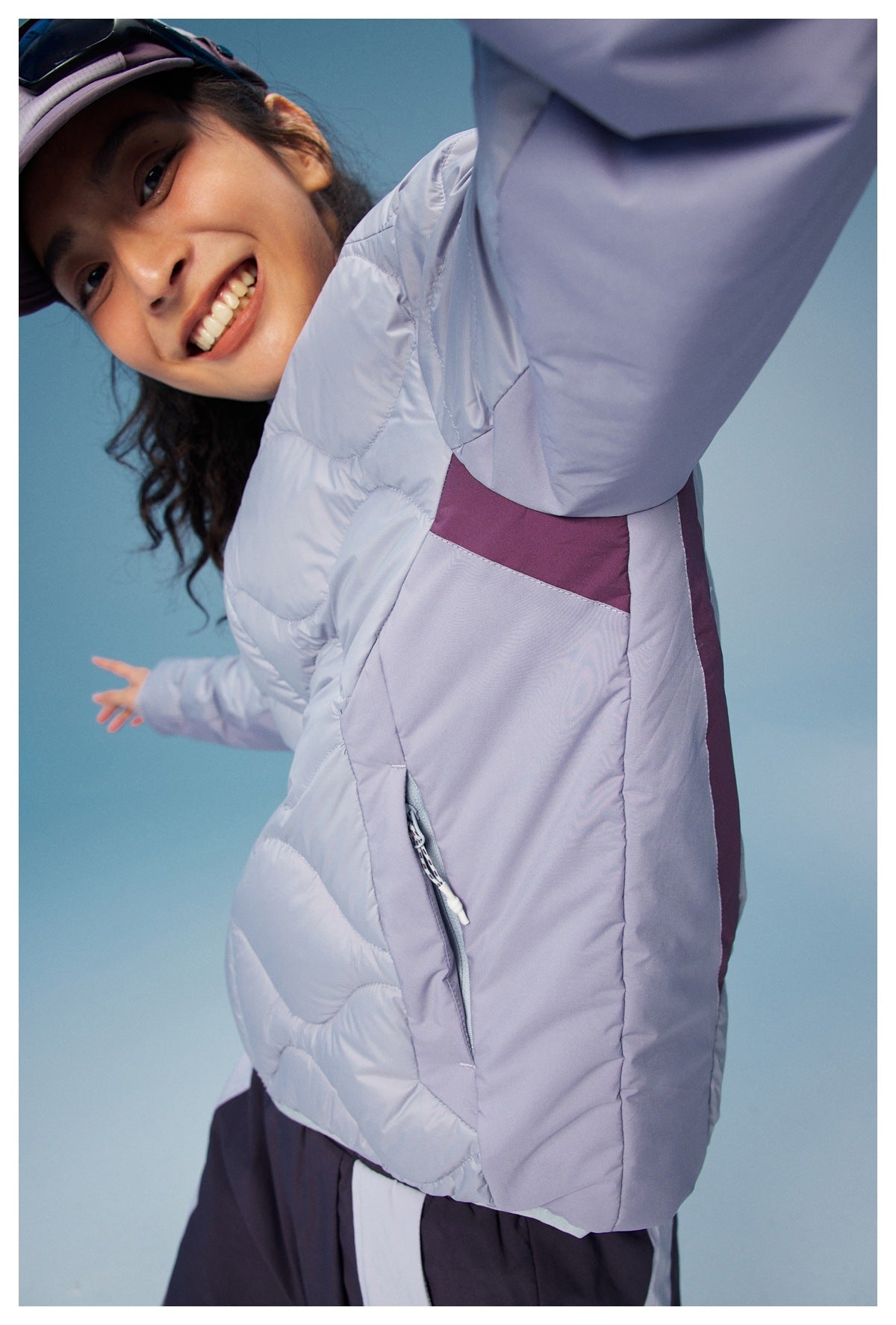 Close view of the jacket's lavender side panel, plum color block, and zippered pocket with a pull cord.