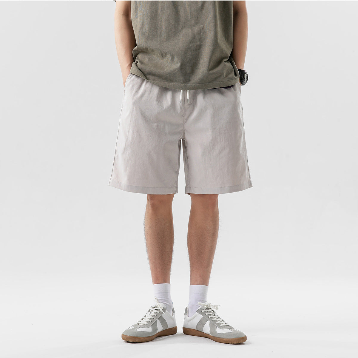 Cropped model wearing light gray drawstring shorts with an olive T-shirt and sneakers, front view.
