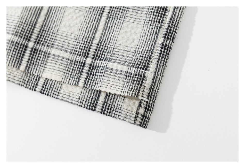 Close-up of the hem and side seam of a cream and black plaid shirt laid flat.