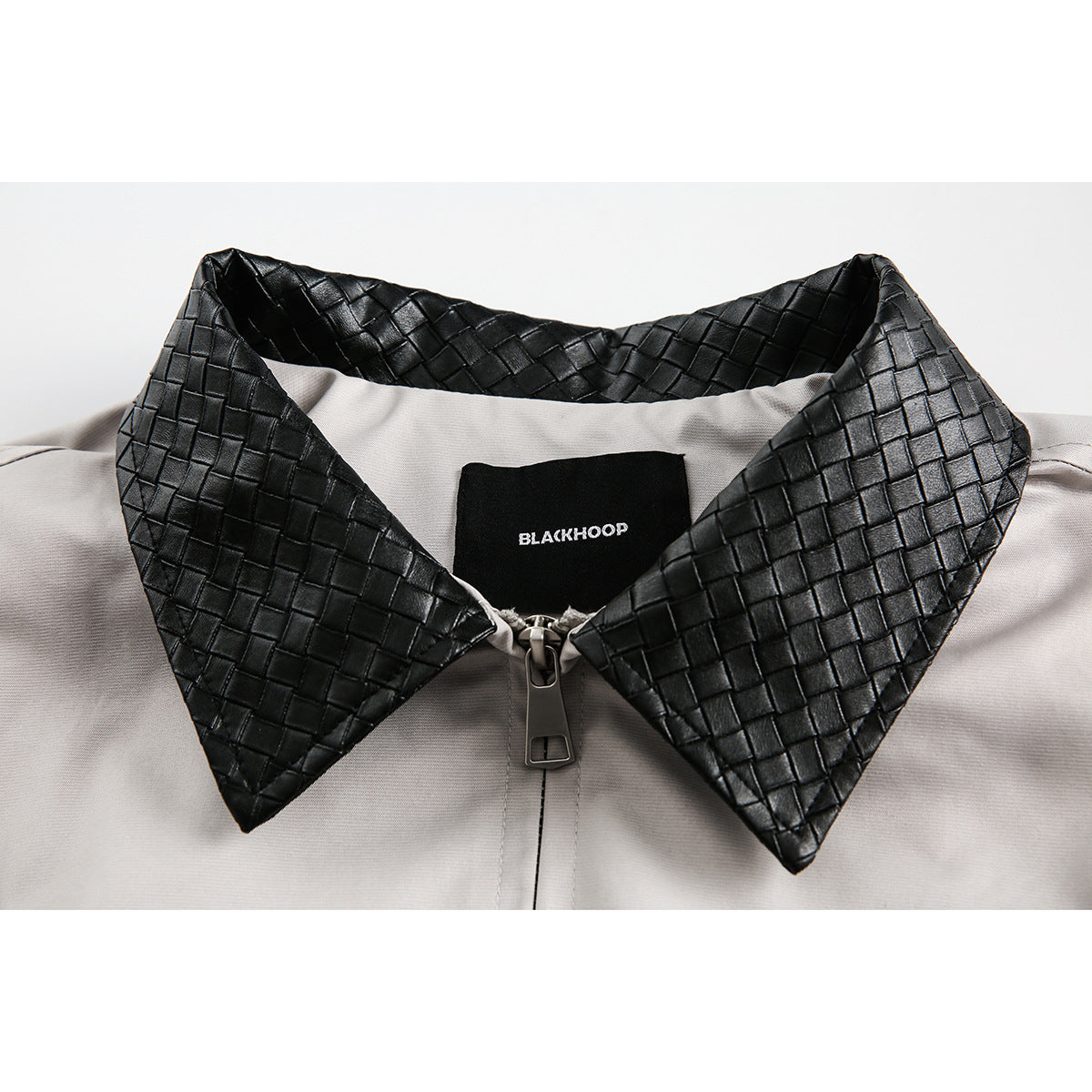 Close-up of a light gray jacket with a black woven-texture collar, front zipper, and sewn-in BLACKHOOP label.