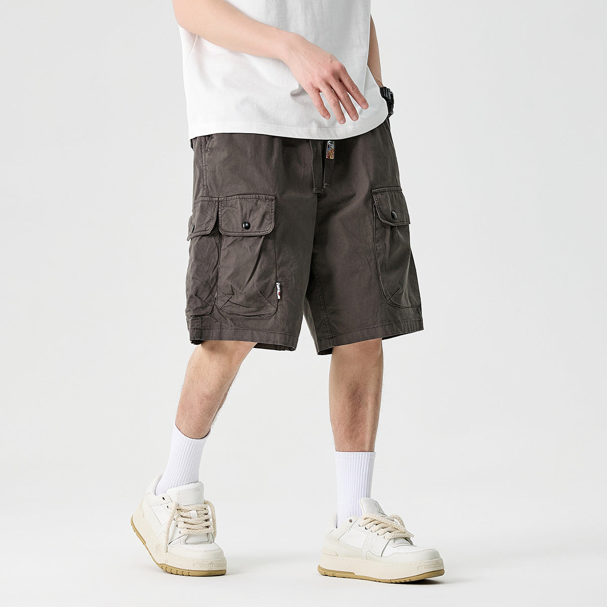 Cropped model wearing charcoal gray cargo shorts with large button-flap pockets and a white T-shirt.