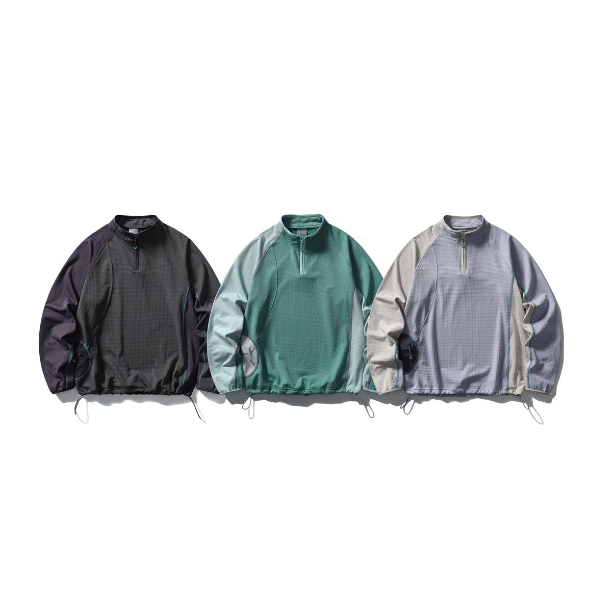 Three quarter-zip pullover tops shown side by side in charcoal, teal, and light lavender with beige sleeves.