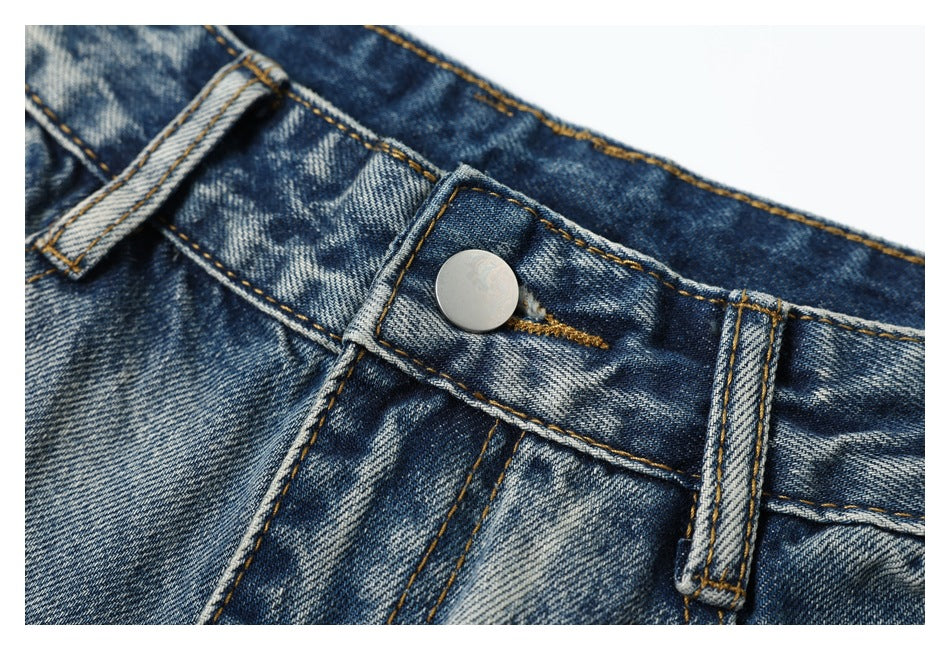 Close-up of the metal button, belt loop and waistband stitching on blue acid-wash jeans.
