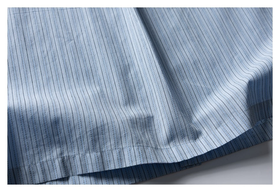 Close-up of the stitched hem and drape of light blue striped fabric.