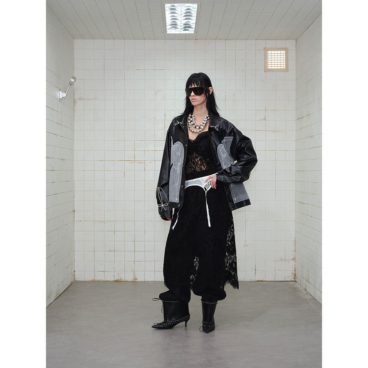 Model wearing a black jacket with gray decorative panels and white stitching, shown with a black lace skirt.