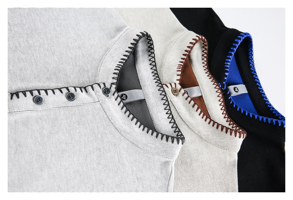 Close-up of overlapping gray, cream and black shirts showing button plackets, contrast stitching and neck labels.