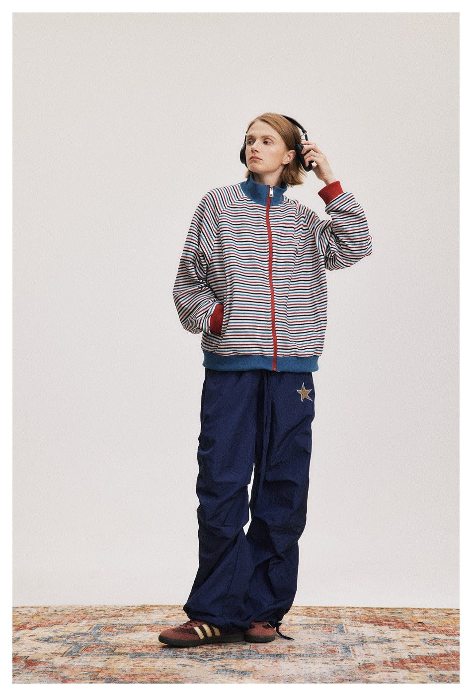 Full-length model wearing a striped zip jacket with blue trim and loose navy pants with a star patch.
