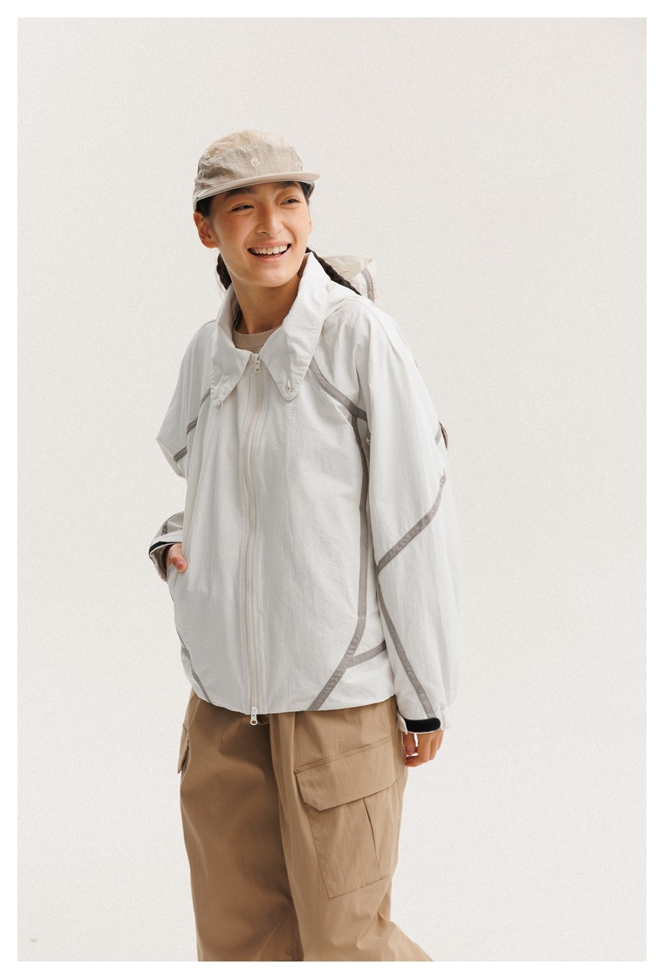 Smiling model in a white zip-front jacket with gray piping and tan cargo pants, shown from the front.