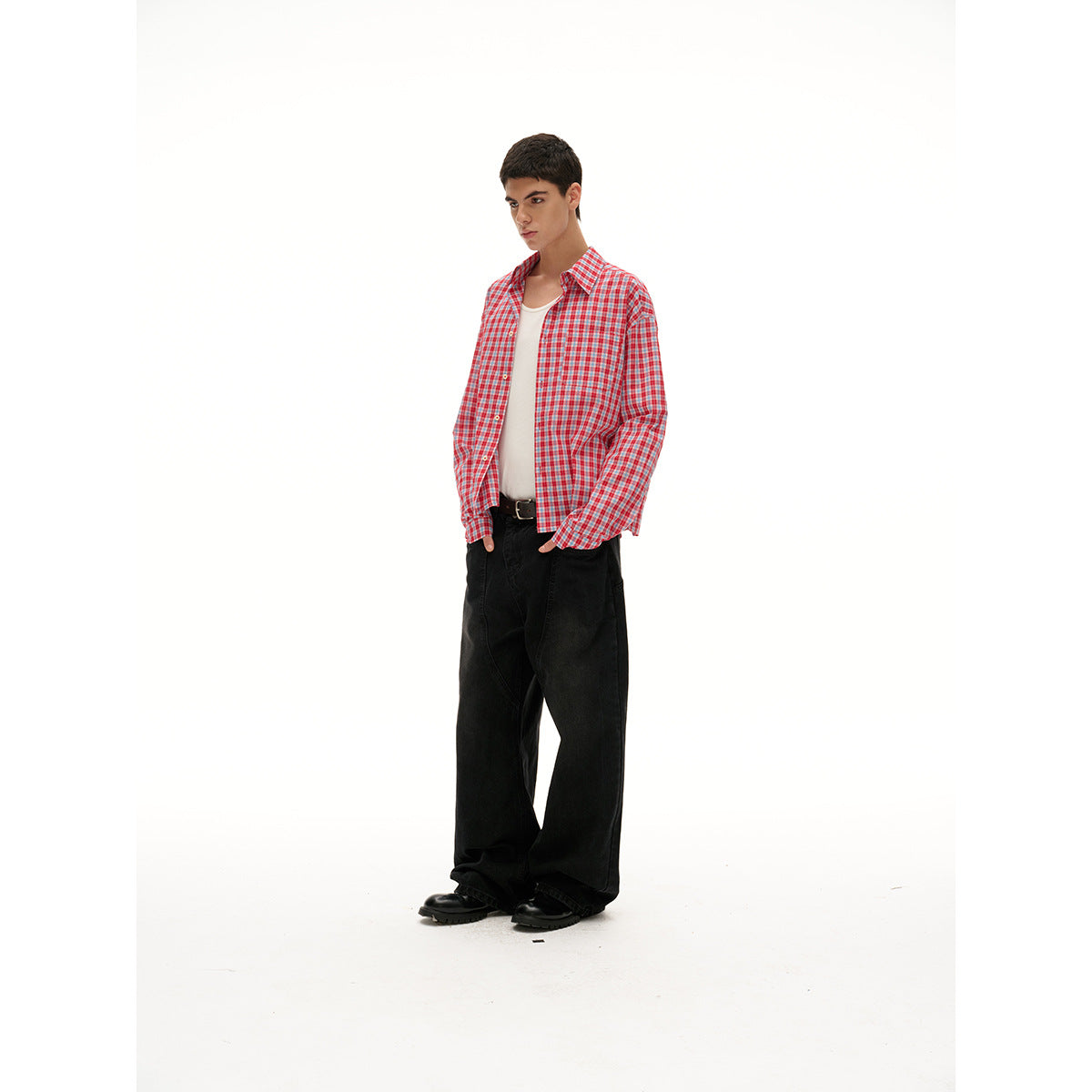 Side view of a model wearing an open red, white, and blue plaid shirt over a white tank with wide black trousers.