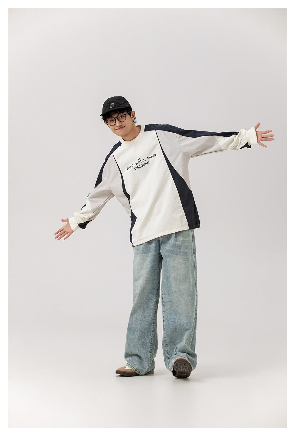 Model wearing an ivory and navy color-block long-sleeve pullover with chest lettering and light-wash wide-leg jeans.