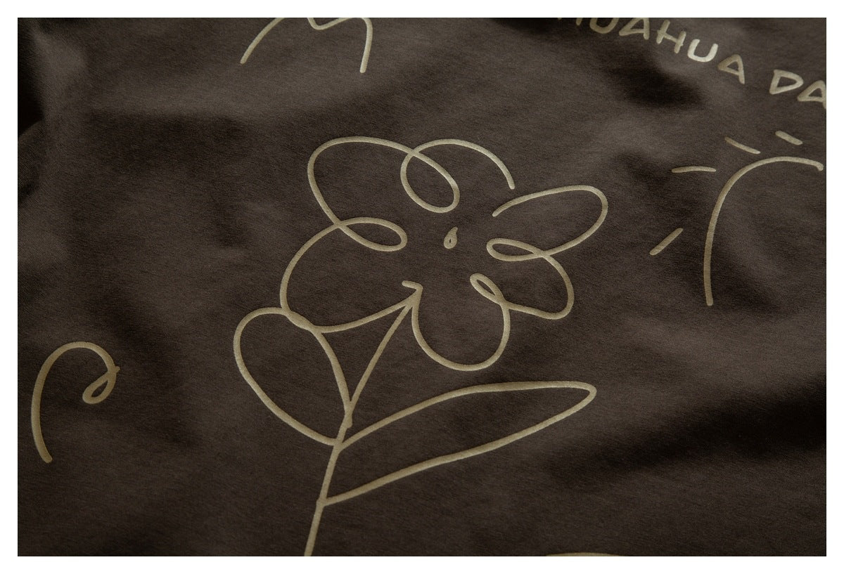 Close-up of a tan line-drawn flower and other graphics printed on dark brown fabric.