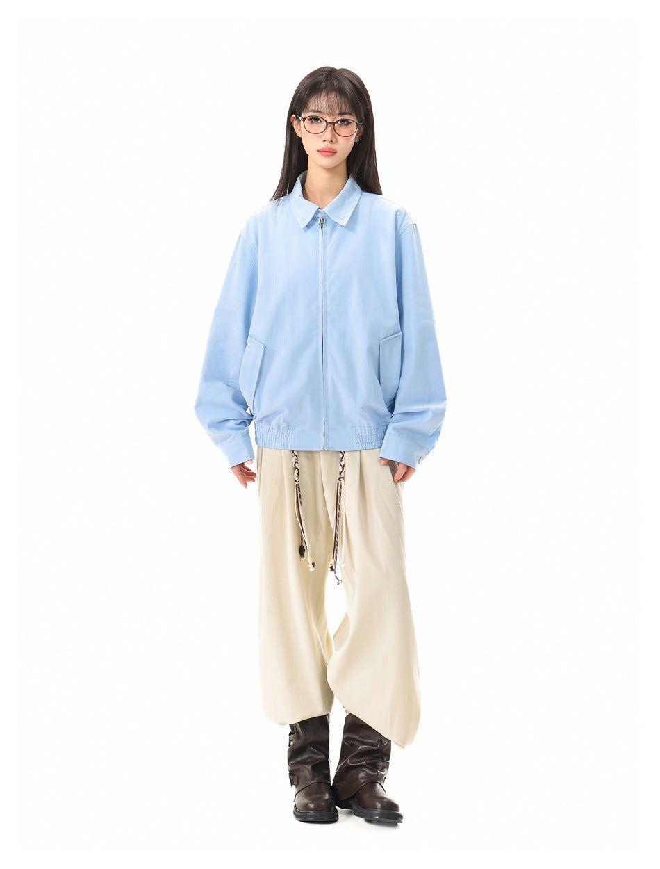 Full-length front view of a model wearing a light blue collared zip jacket with front pockets and cream trousers.